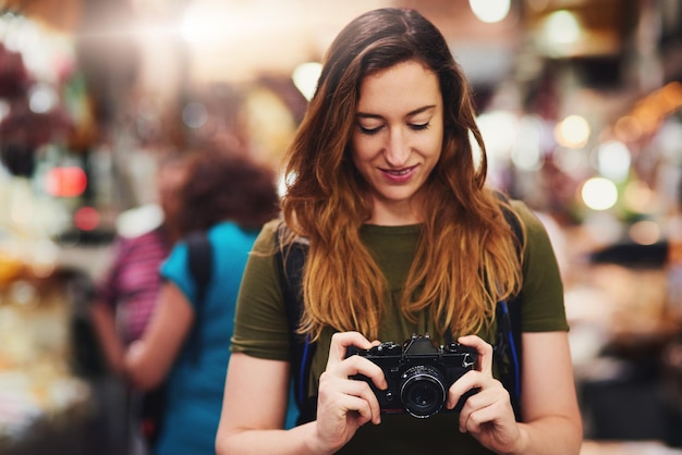 Es hora de hacer lo que mejor hacen los turistas Foto de una joven alegre sosteniendo una cámara y mirando la pantalla mientras está de pie en un mercado al aire libre durante el día