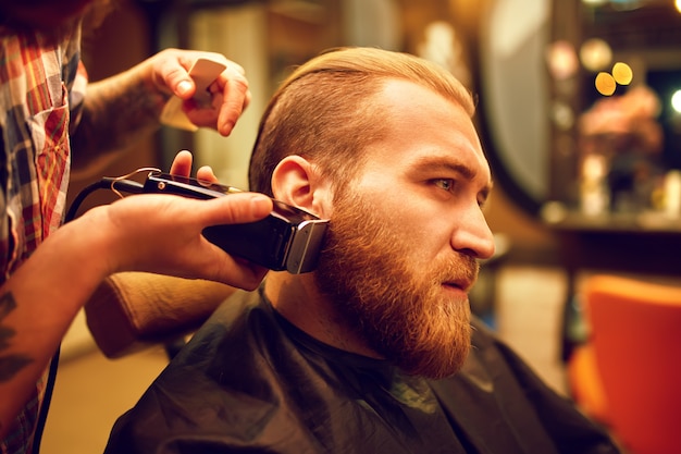 Es hora de un nuevo peinado. Apuesto joven barbudo vino al barbero para cortarse el pelo. Estilo hipster. El concepto de moda y belleza.