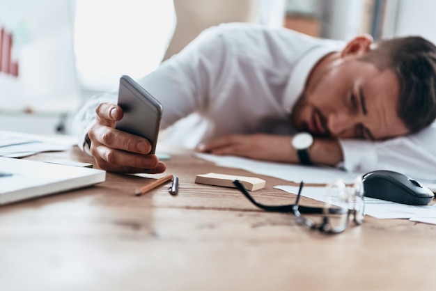 Es hora de ponerse a trabajar. Joven cansado en ropa formal acostado sobre el escritorio mientras trabaja hasta tarde