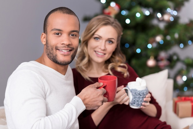 Foto es la hora del té. apuesto hombre guapo positivo sosteniendo una taza roja y mirándote mientras tomas el té