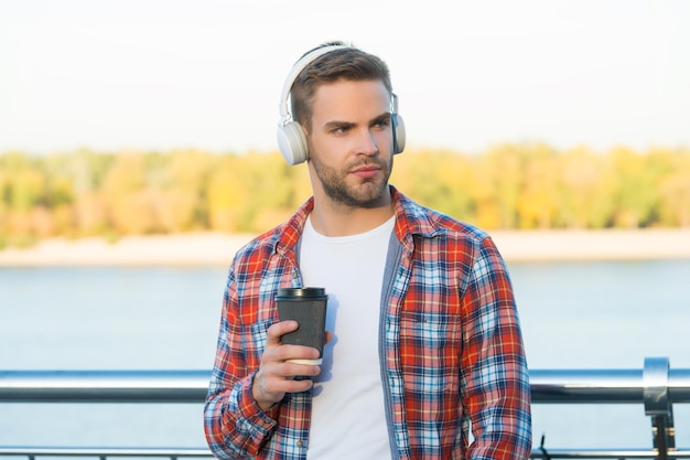 Es hora de tomar un descanso hombre en auriculares escuchar música estilo elearning mientras bebe café calidad de sonido buenos días beber chico sin afeitar con taza de café al aire libre masculino casual moda hipster