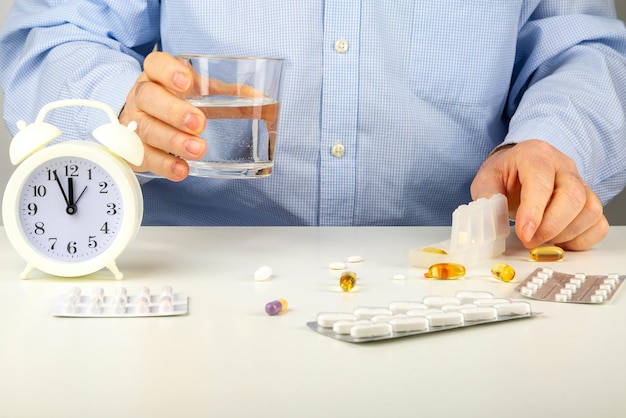 Es hora de tomar medicamentos, un hombre toma pastillas con un vaso de agua y un reloj sobre la mesa