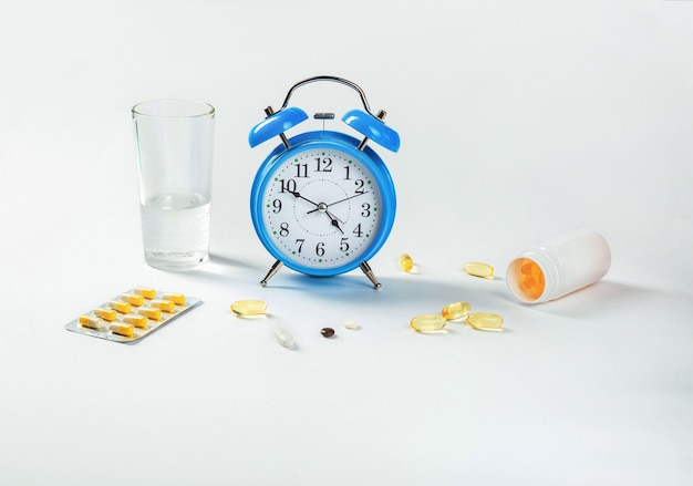 Es hora de tomar las pastillas. Un reloj despertador muestra la hora de tomar el medicamento y, al lado, píldoras médicas.