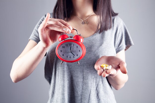 Es hora de tomar su medicación. niña sosteniendo pastillas y despertador