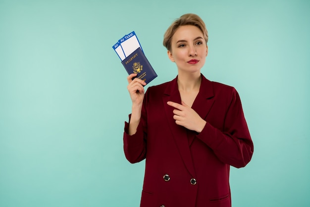 Es hora de viajar. Una mujer sonriente de moda moderna en traje rojo apuntando a los billetes de avión y un pasaporte en la mano.