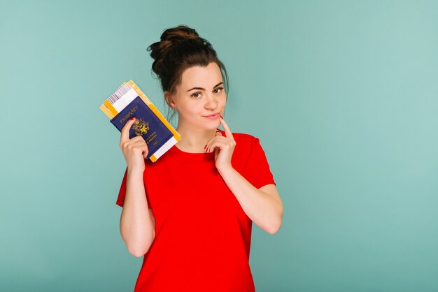 Es hora de viajar. Una mujer sonriente de moda moderna en vestido rojo con billetes de avión y un pasaporte en la mano.