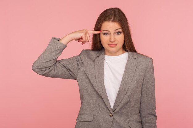 Esta es una idea loca Retrato de una mujer en traje de negocios que muestra un gesto estúpido con el dedo en la sien disgustada con una broma tonta e imprudente fuera de la mente Foto de estudio aislada en un fondo rosa