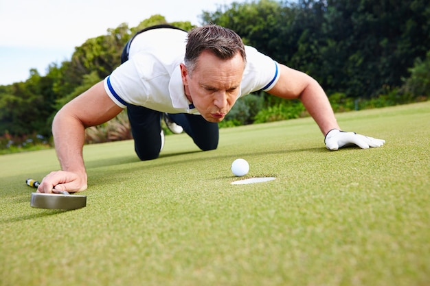 Es ist kein Schummeln, wenn es niemand sieht Aufnahme eines gutaussehenden Mannes, der versucht, seinen Golfball in das Loch zu blasen