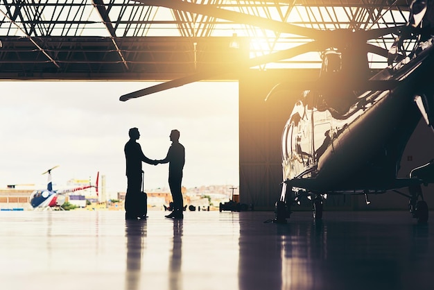 Es ist schön, sich endlich im Geschäft zu treffen Ganzkörperaufnahme von zwei nicht erkennbaren Geschäftsleuten, die sich die Hände schütteln, während sie in einem Hangar am Flughafen stehen