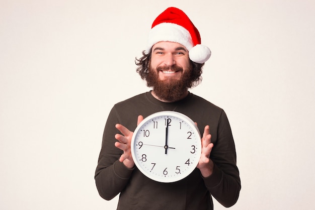 Es ist Weihnachtszeit. Lächelnder bärtiger Mann mit Feiertagshut zeigt eine Uhr.