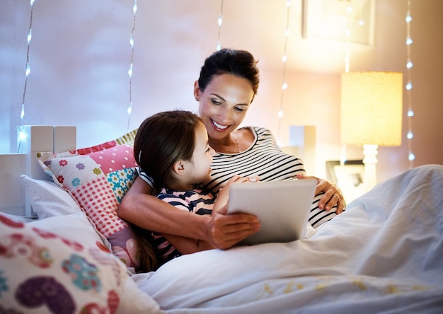 Es ist Zeit für eine weitere Aufnahme einer attraktiven jungen schwangeren Frau, die ihrer Tochter auf einem Tablet eine Gute-Nacht-Geschichte vorliest