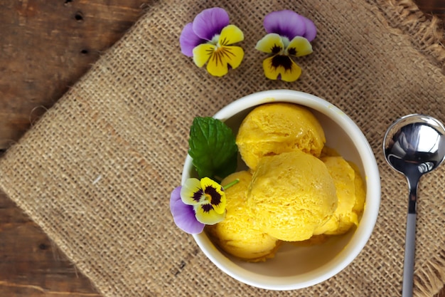 Es krim mangga Sorbete de helado de mango con hojas de menta y flor comestible pensamiento viola