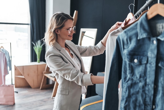 esto es lo que necesito. Atractiva mujer joven en ropa casual elegante eligiendo ropa del rango