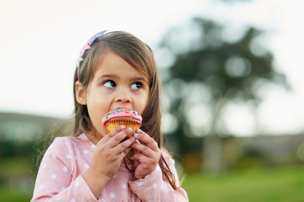 Esto es más que delicioso Captura recortada de una niña pequeña disfrutando de un pastelito afuera