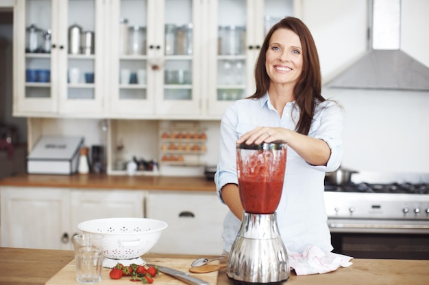 Esta es mi mezcla favorita para el desayuno. Una mujer atractiva usando una licuadora para hacer un batido de frutas.