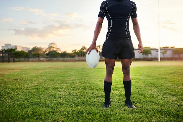 Esta es mi zona de confort Captura recortada de un deportista irreconocible parado solo y sosteniendo una pelota de rugby durante una práctica matutina