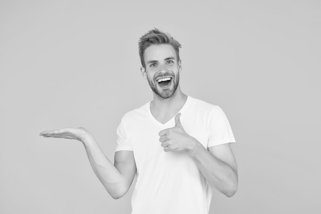 Este es el modelo de moda más seguro con camisa blanca. Hombre feliz que presenta el producto. Chico feliz. Toca su vello facial.