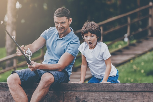 ¡Es un pez grande! Feliz padre e hijo pescando juntos mientras el niño pequeño se ve emocionado y mantiene la boca abierta