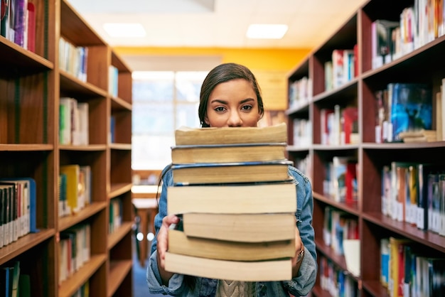 Es una pila de conocimiento Retrato de un estudiante universitario sosteniendo una pila de libros en la biblioteca del campus