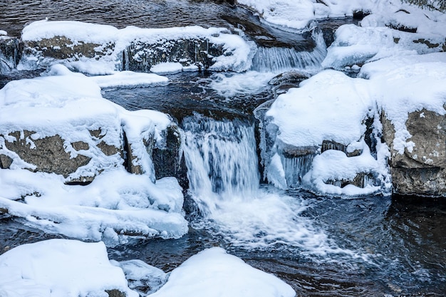 Es schneit auf einem Fluss mit schneebedeckten Steinen