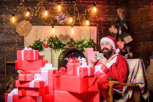 Es la temporada para ser un hombre barbudo alegre con una caja de regalo regalos de navidad ventas de navidad feliz navidad feliz año nuevo disfraz de santa rojo hombre feliz bebe té leche para santa