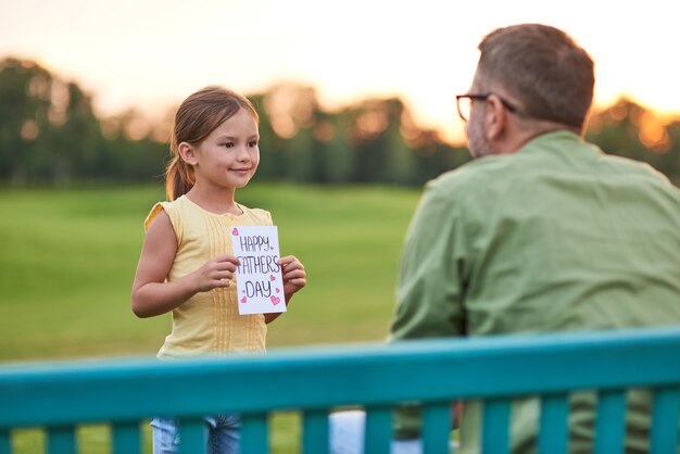 Esto es para ti, papá, linda niña saludando a su papá y dándole una postal hecha a mano.