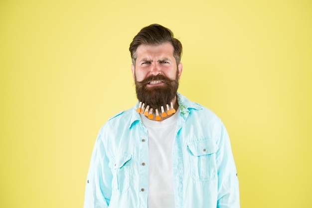 Es tut so weh. individuelle frisur für männer. Mann Wäscheklammer am Bart. Brutaler Hipster mit Wäscheklammerherzen. bärtiger mann lässiger stil gelber hintergrund. Valentinstag. Haare trocknen im Friseur.