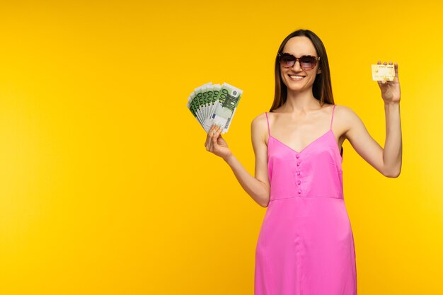 Esbelta chica española con un vestido rosa y gafas de sol con billetes de cien euros y una tarjeta de crédito