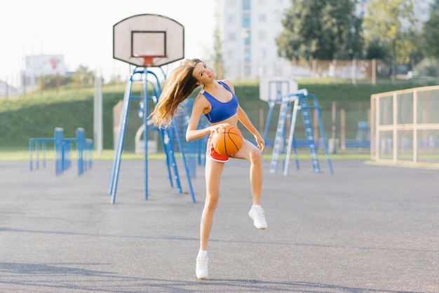 Esbelta garota atlética em tiros curtos e top joga com uma bola de basquete no playground