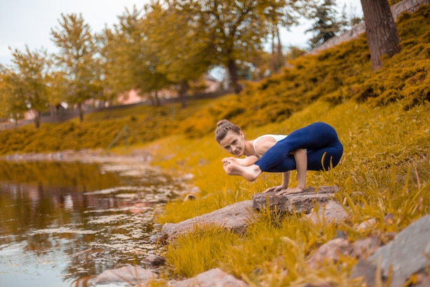 Esbelta joven morena yogui realiza desafiantes ejercicios de yoga en la hierba verde en otoño