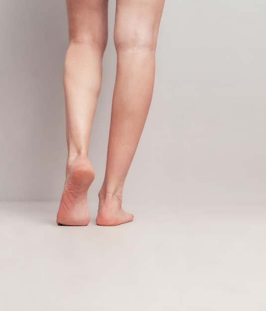Esbeltas piernas femeninas levantadas sobre los dedos de los pies sobre un fondo gris claro