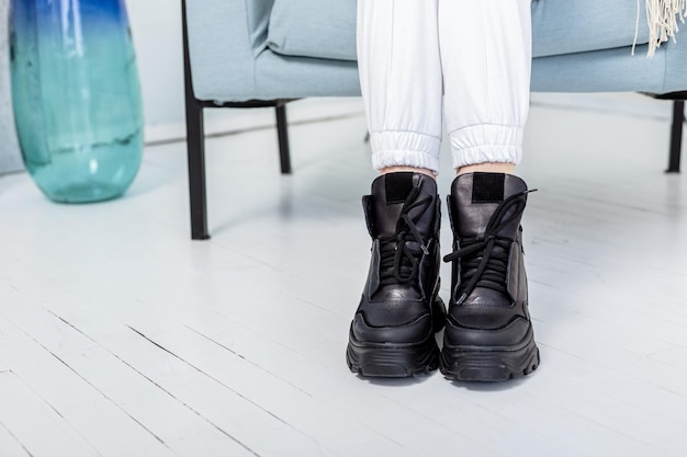 Esbeltas piernas femeninas en pantalones blancos, zapatillas de deporte de cuero negro. Nueva colección de zapatos casual de mujer