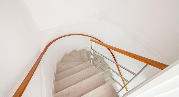 Escada em espiral com escadas brancas e corrimão de madeira na parede dentro de uma casa