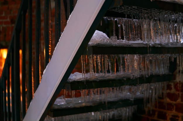 Escada externa ao anoitecer coberta de gelo e pingentes de gelo iluminados por uma janela atrás dela