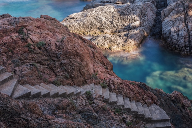 Escada rochosa, rocha iluminada e mar esmeralda