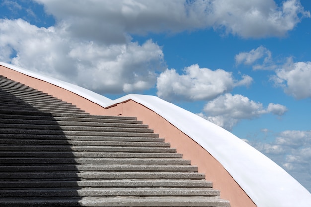 Escadaria concreta contra o céu azul e as nuvens.