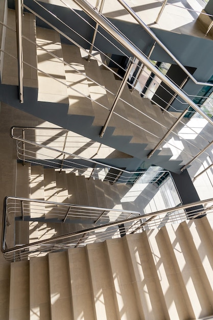 Escadas em um prédio de escritórios de concreto em tons neutros cobertos com ladrilhos de cerâmica com trilhos metálicos brilhantes