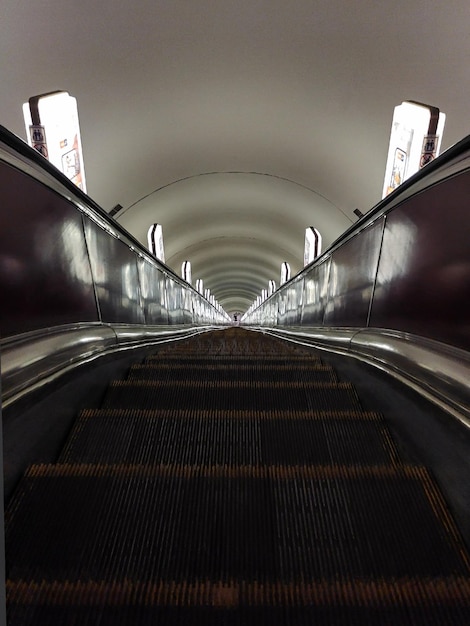 Escadas rolantes vazias do metrô com trilhos e lâmpadas nas laterais