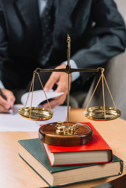 Foto escala de la justicia de oro en la pila de libros frente al abogado que firma el documento