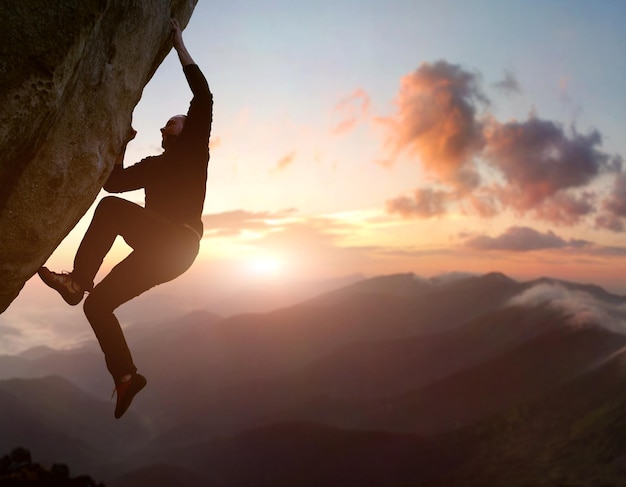 Escalada de roca. Escalador masculino tratando de permanecer en roca desafiante, superando obstáculos. Montaña y amanecer en el fondo