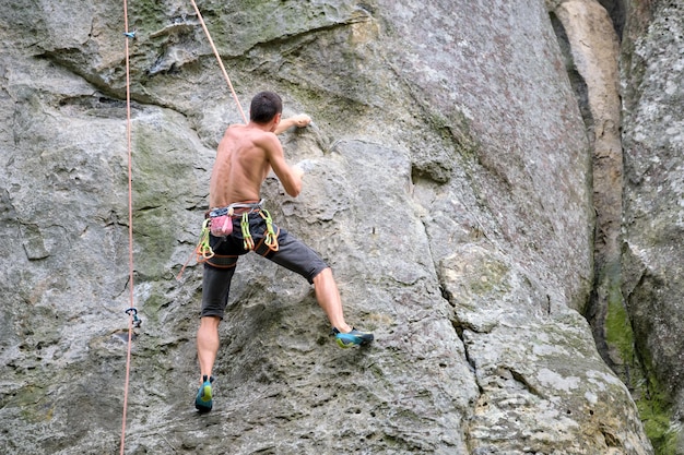 Escalador decidido trepando por la empinada pared de la montaña rocosa. Deportista superando ruta difícil. Participar en el concepto de hobby de deportes extremos y escalada en roca.