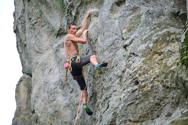 Escalador decidido trepando por la pared empinada de la montaña rocosa Deportista superando ruta difícil Participar en deportes extremos y el concepto de pasatiempo de escalada en roca