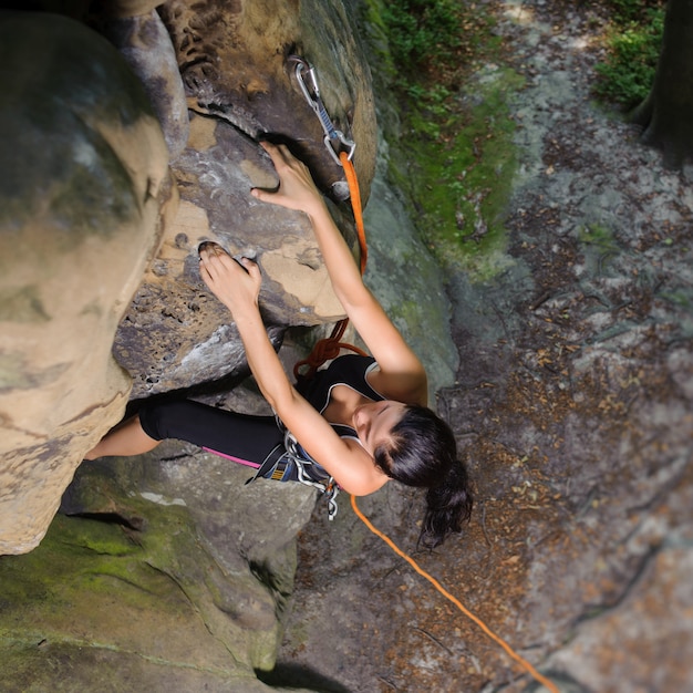 Escalador femenino que sube la roca grande en naturaleza con la cuerda