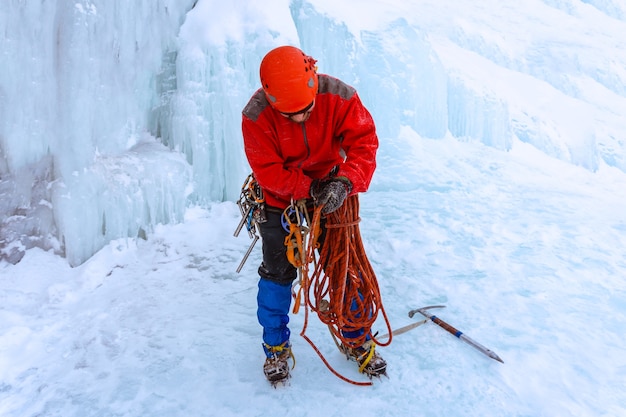 Escalador de hielo de pie sobre la nieve debajo del glaciar está preparando una cuerda para escalar