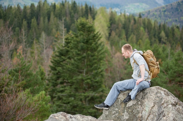 Escalador masculino con mochila marrón en la cima de la roca