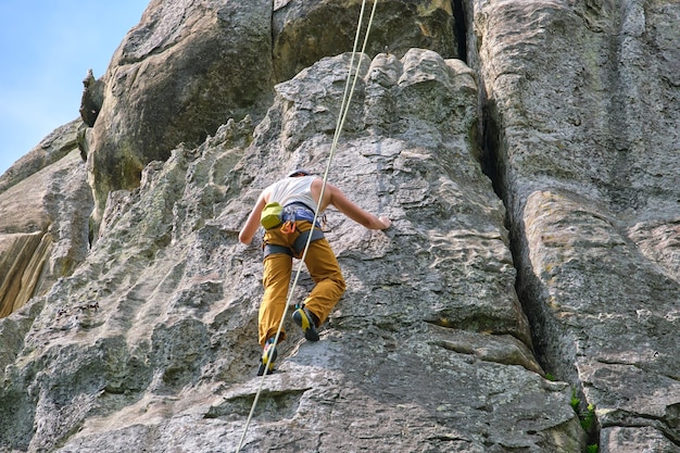 Escalador resuelto trepando por la empinada pared de la montaña rocosa. Deportista superando ruta difícil. Participar en deportes extremos y el concepto de hobby de escalada en roca.