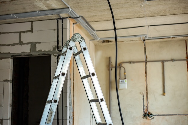 Escalera de aluminio y cables eléctricos tendidos en corrugado protector instalado en el techo