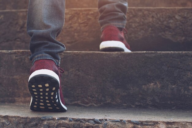 Escalera. Cerrar piernas jeans y zapatos zapatillas rojo de hombre joven inconformista Una persona caminando subiendo las escaleras en la ciudad moderna, sube la escalera, éxito, crece. Sol por la mañana.