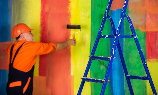 Foto escalera del hombre pintor. para hacer reparaciones. hombre en ropa de trabajo pintando la pared en una habitación vacía. pintor en mono y gorra con bote de pintura. fachada de pintura de trabajador constructor. trabajos de aislamiento térmico.