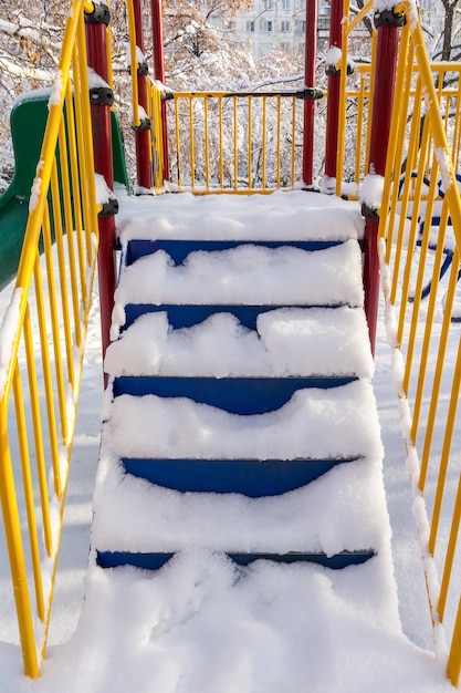 La escalera de metal del tobogán infantil está cubierta de nieve caída